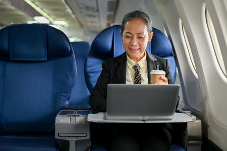 A successful senior Asian businesswoman working on her business tasks on her laptop during the flight for her business trip. Businesspeople and transportation conceptの写真素材