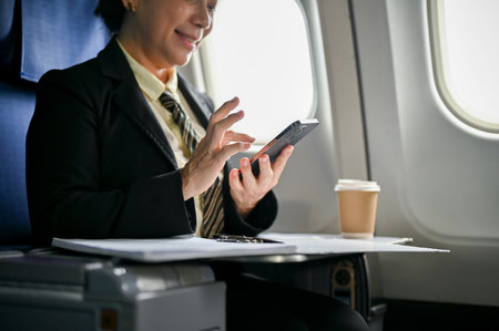 A happy and relaxed senior Asian businesswoman using her smartphone during the flight for her business trip.の写真素材