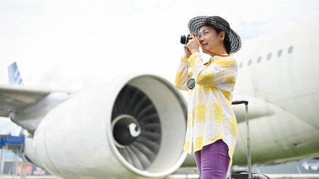 A happy and attractive senior Asian female tourist taking pictures with her film camera at the airport. summer vacation, tourist, trip, holiday, airplaneの写真素材