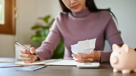Close-up image of an Asian woman sitting at a table checking her electric bills and planning her household expenses.の写真素材