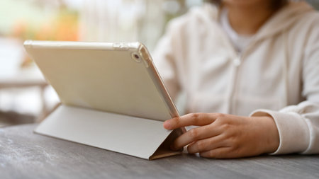 Close-up image of an Asian female freelancer in a white sweater using her digital tablet while...