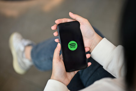 Chiang Mai, Thailand - July 17 2023: A woman holding an iPhone14 with a Spotify logo on screen over blurred background. close-up imageのeditorial素材