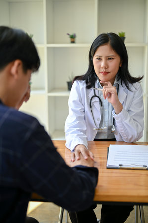 A professional Asian female doctor is touching a patient's hand to provide comfort and reassurance during the medical checkup at a hospital.の写真素材