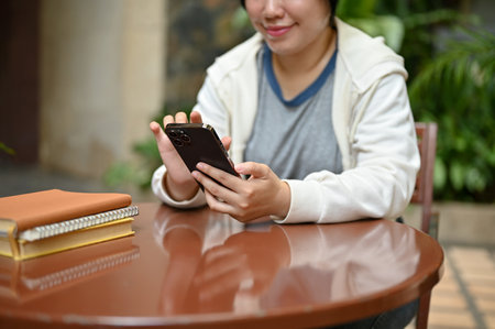 Close-up image of a happy young Asian woman in casual clothes using her smartphone while relaxing at...