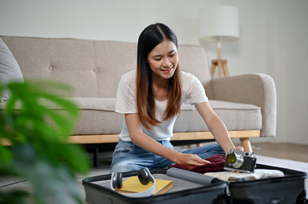 A happy and beautiful Asian woman is preparing her belongings and packing her luggage in her living...