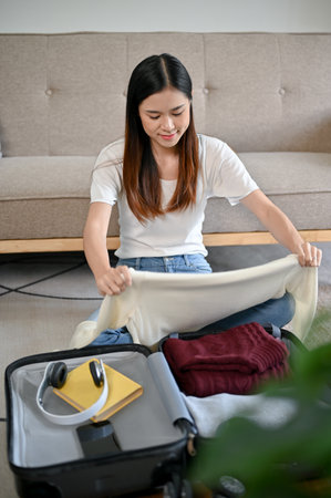 A beautiful Asian woman is folding her clothes, preparing her belongings, and packing her suitcase...