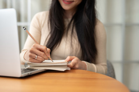 Close-up image of a smart Asian female college student writing in her notebook, doing homework, or lecturing while studying online at home.の写真素材