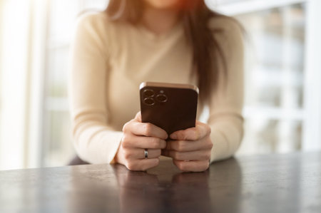 Close-up image of a woman sitting at a table indoors and using her smartphone. chat, message, text, social media, applicationの写真素材