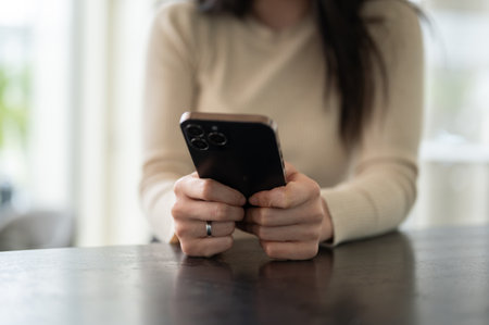 Close-up image of an Asian woman in casual clothes sits at a table and uses her smartphone. People and technology conceptの写真素材