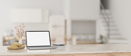 A modern home workspace with a laptop white screen mockup, books, and decors on a luxury white marble table with a blurred modern white kitchen as a background. 3d render, 3d illustrationの写真素材
