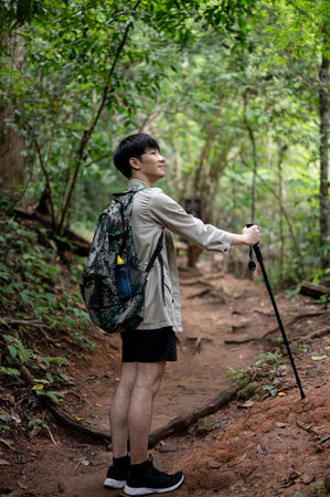 A portrait of a handsome and happy Asian male hiker with a backpack and trekking gear walking along the nature mountain path, exploring the forest, and enjoying his hiking trip.の写真素材
