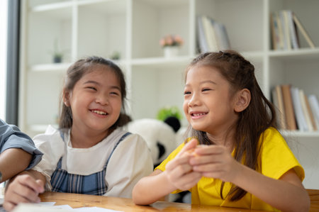 Two adorable young Asian girls are enjoying talking on a small break in a classroom together....