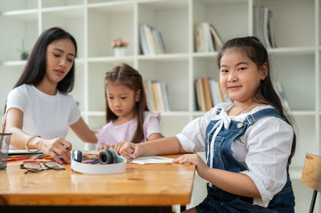 An adorable young Asian girl is sitting in the classroom with a teacher and her friends, smiling and looking at the camera. Kids, elementary school students, Childrenの写真素材