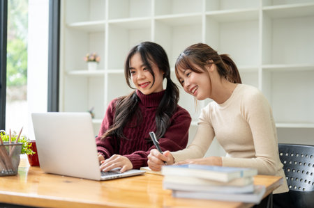Two pretty Asian female friends are working remotely at a coffee shop together on the weekend. college students, friendship, colleaguesの写真素材