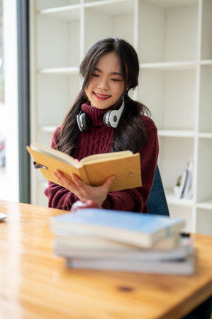 A portrait of a beautiful young Asian female in a cozy red sweater is reading a book at a table in the coffee shop.の写真素材