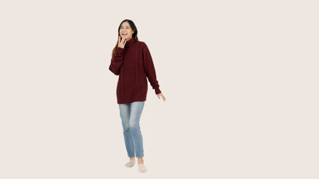 An attractive and cheerful young Asian woman in a red sweater stands against an isolated white...
