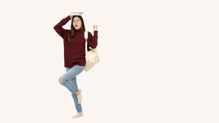 A cheerful and determined Asian female college student is holding books over her head and showing...