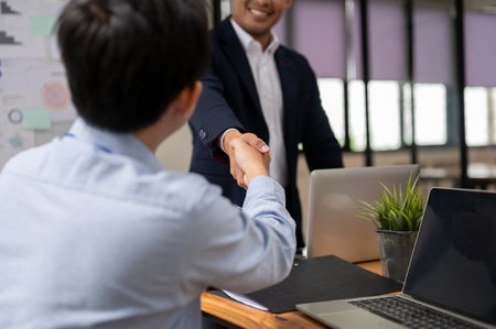 Close-up image of a professional and successful Asian businessman or male boss is shaking hands with a male employee during the meeting. teamwork, congratulations, welcome, agreementの写真素材