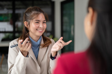 A cheerful Asian businesswoman is talking with her colleague in the office. A professional businesswoman is in the meeting with a client.の写真素材