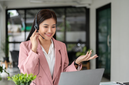 A beautiful Asian female call centre operator with a headset is having a conversation with a...