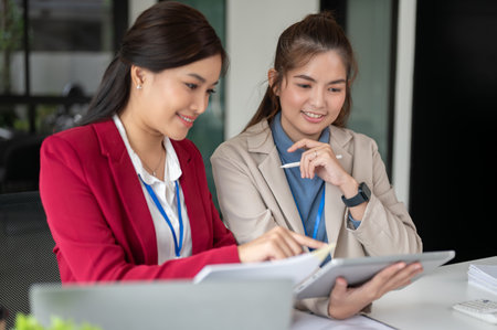 Two professional and attractive Asian businesswomen are examining a project's details and working on it together at a table in the office. co-working, teamwork, coworkerの写真素材