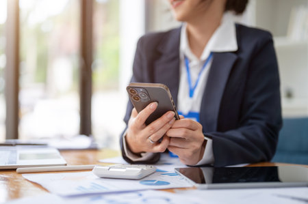 Close-up image of a beautiful Asian businesswoman or female accountant using her smartphone at her desk. connection, internet, mobile applicationの写真素材