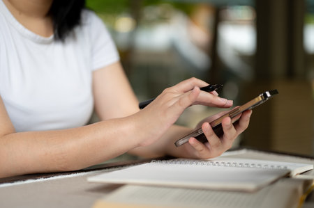 Close-up image of a female freelancer typing on her smartphone screen, chatting, sending messages while sitting at a table in a coffee shop.の写真素材