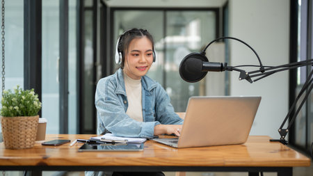 A beautiful Asian female podcaster or radio host working in her studio, speaking into a microphone,...