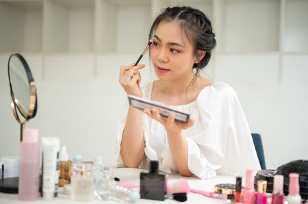 A beautiful and charming Asian woman applies eye shadow to her eyelids, getting ready at her vanity dress in her room. Lifestyle conceptの写真素材