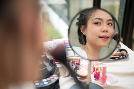Close-up image of a beautiful and charming Asian woman looking at the mirror while applying makeup in her room. Beauty blogger, influencer, makeup artistの写真素材