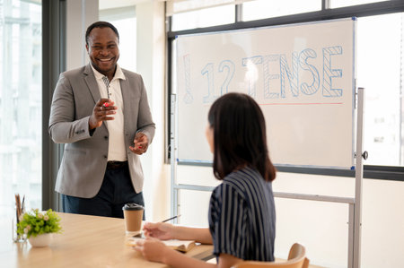A friendly and professional African American male teacher teaches English, explaining English tense and grammar for Asian students at a language school. Education and diversity conceptの写真素材