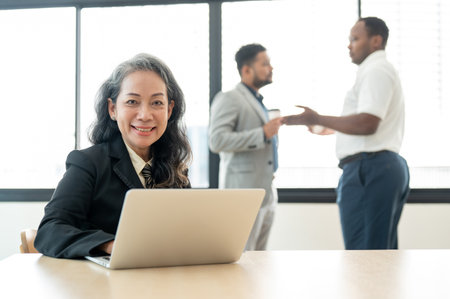 A professional and successful senior Asian businesswoman or female boss sits at a table with her laptop in a meeting room.の写真素材