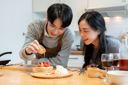 A handsome young Asian man is pouring syrup on pancakes, enjoys cooking pancakes with his girlfriend in the kitchen on the weekend.の写真素材