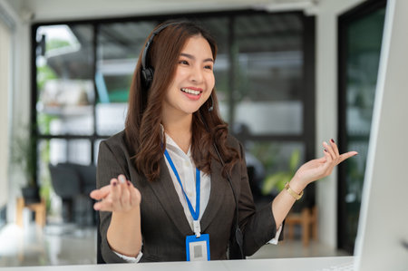 An attractive and cheerful Asian female call centre agent or telemarketer operator with a wireless...