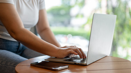 Close-up image of a female freelancer working remotely at a coffee shop, using her laptop to manage...