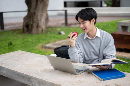A happy and handsome young Asian male college student is doing his homework or preparing for the exam in a campus park. Education conceptの写真素材
