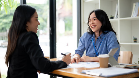 An attractive and cheerful young Asian businesswoman or female financial consultant enjoys talking with her client during the an informal meeting in the office.の写真素材