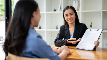 A gorgeous and professional Asian businesswoman or sales agent is showing the contract to a female client and explaining the contract agreement while having a meeting in the office.の写真素材