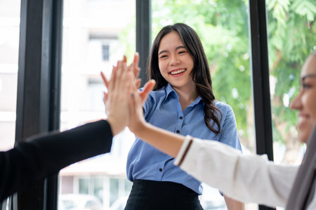A beautiful and cheerful Asian businesswoman is putting her hand up or giving high fives to her team...