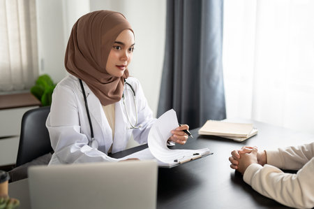 A beautiful and professional Asian Muslim female doctor is consulting a surgery plan and treatment plan with a patient in an examination room at a hospital. Medical worker conceptの写真素材