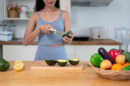 Cropped image of a beautiful and fit Asian woman in gym clothes cutting an avocado and preparing her healthy breakfast in the kitchen before going to the gym.の写真素材