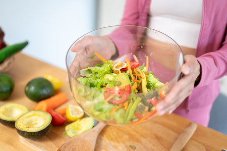 Close-up image of a woman in sportswear holding a bowl of healthy fresh salad over the kitchen table. Healthy food, diet meals, high nutrition, wellbeing, cookingの写真素材