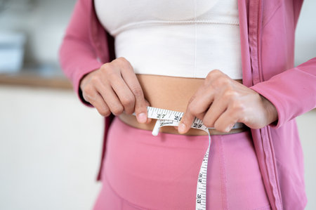 Close-up image of a healthy and slim woman in sportswear measuring her waist with a measuring tape....