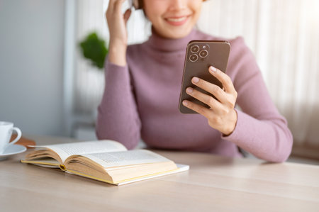 Close-up image of a happy young Asian woman is choosing a music playlist on her smartphone and enjoying listening to music while sitting at a table in her room.の写真素材