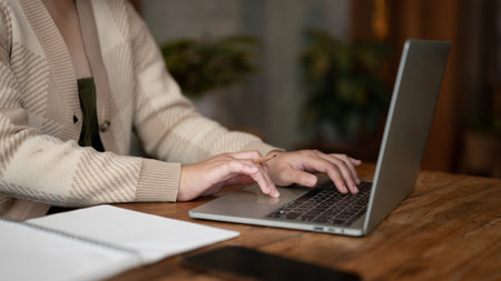 Close-up image of a woman working remotely at a coffee shop, working on her laptop, typing on laptop keyboard. Urban lifestyle conceptの写真素材