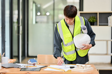 A professional and focused Asian male engineer or architect with a safety helmet is checking the...