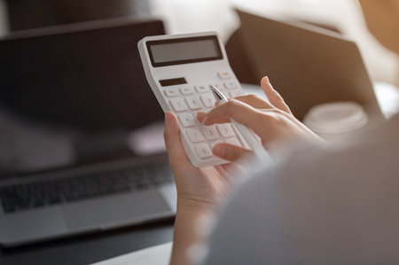 Close-up rear view image of a businesswoman or female accountant using a calculator at her desk. calculating, financial, money, accountingの写真素材