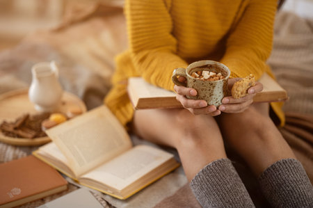 Close-up image of a woman in a cosy sweater and winter socks sitting on a bed with a cup of hot cocoa in her hands. Winter, autumn, leisure and lifestyleの写真素材