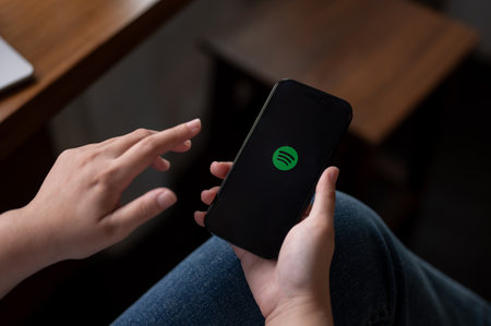 Chiang mai, Thailand - Oct 05 2023: A woman sitting indoors and using a Spotify application through...
