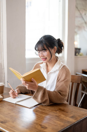 A beautiful and focused young Asian female college student in a comfy sweater doing her homework,...